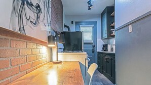 Eine schmale Küche mit Backsteinwand, einem Holztisch und einem weißen Stuhl.