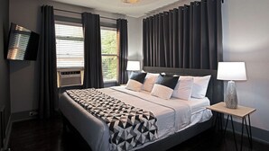Ein modernes Hotelzimmer mit einem großen Bett, einem Flachbildfernseher, einem Nachttisch mit Lampe und einem Vorhangfenster.