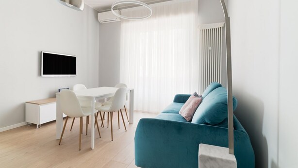 A modern living room with a teal sofa, a dining area with white chairs, a flat-screen TV, and a minimalist design. - GuestHost - Bright apartment of about 85 sqm, able to accommodate up to 5 people, located on the mezzanine floor of a building (NO elevator - there are some steps to climb).The property is located in a residential area of ​​Milan, full of services an (Milan)