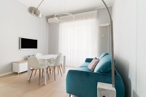 Un salon moderne avec un canapé de couleur turquoise, un coin repas avec des chaises blanches, un téléviseur à écran plat et un design minimaliste.