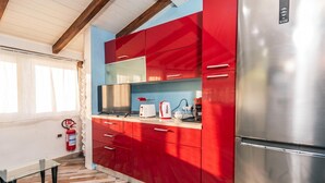 A compact kitchen with red cabinets, a stainless steel refrigerator, and a small countertop with a toaster and kettle. - La Rosa dei Venti (Sorso)