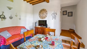 Ein gemütliches Zimmer mit einer Couch, einem Esstisch mit bunten Tischdeko, einem Holzschrank und einer Wanduhr.