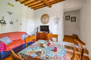 Um quarto acolhedor com um sofá, uma mesa de jantar com toalha de mesa colorida, um armário de madeira e um relógio de parede.