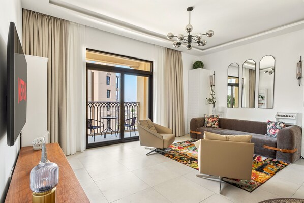 Un salon moderne avec un canapé, des fauteuils, un téléviseur et un balcon offrant une vue sur les immeubles.