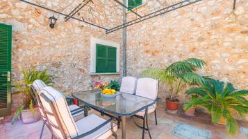 Un patio con pareti in pietra, un tavolo e sedie in vetro, circondato da piante in vaso.