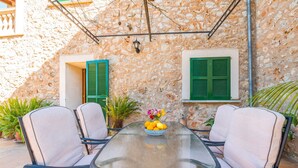 A glass-top table with four chairs, a bowl of fruit, and two green shutters on a stone wall. - Ses Roques in Santa Maria del Cam (Santa Maria del Camí)