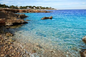 Un paysage côtier avec une eau d’un bleu limpide, une côte rocheuse et des bâtiments en arrière-plan.