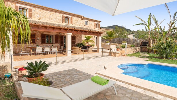 A stone building with a pool, outdoor seating, and potted plants.