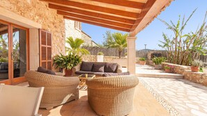 An outdoor patio with wicker furniture, a stone wall, and potted plants.