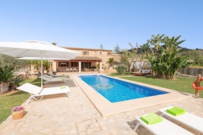 A swimming pool with lounge chairs and umbrellas, surrounded by a stone patio and lush greenery. - Can Lliganya in Santa y (Felanitx)