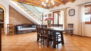 A dining area with a wooden table and chairs, a staircase with a stone wall, and a chandelier.