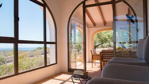 A sunlit room with large windows, a view of the outdoors, and a small table with books. - Los Lobitos in Cumbre del Sol (Javea)