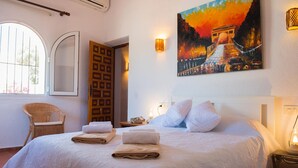 A neatly made bed with folded towels, a painting of a bridge, a chair, and a window with bars. - Los Lobitos in Cumbre del Sol (Javea)
