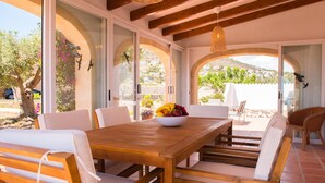 A wooden dining table with white cushioned chairs, a bowl of fruit, and a wicker hanging light fixture. - Los Lobitos in Cumbre del Sol (Javea)