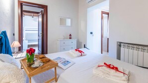 A hotel room with a bed, a bedside table with a tray of croissants, a vase of red flowers, and a framed picture. - Gli Allori in Golfo Aranci (Golfo Aranci)