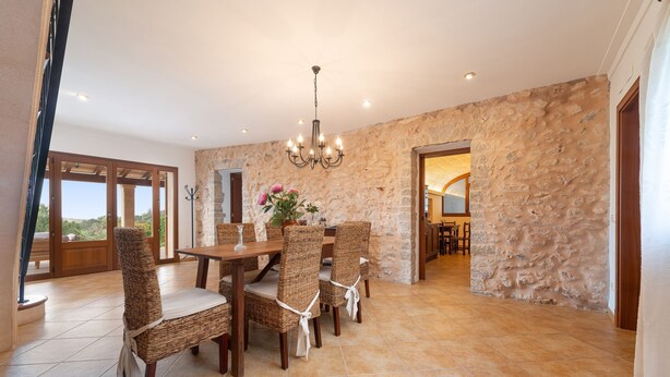 Comedor con pared de piedra, una araña y vistas a través de amplios ventanales.