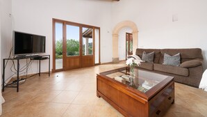 Una sala de estar con televisor, mesa de centro, sofá y una mesa de vidrio con adornos.