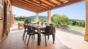 Un patio exterior con una pérgola de madera, una mesa preparada para comer y vistas del paisaje circundante.