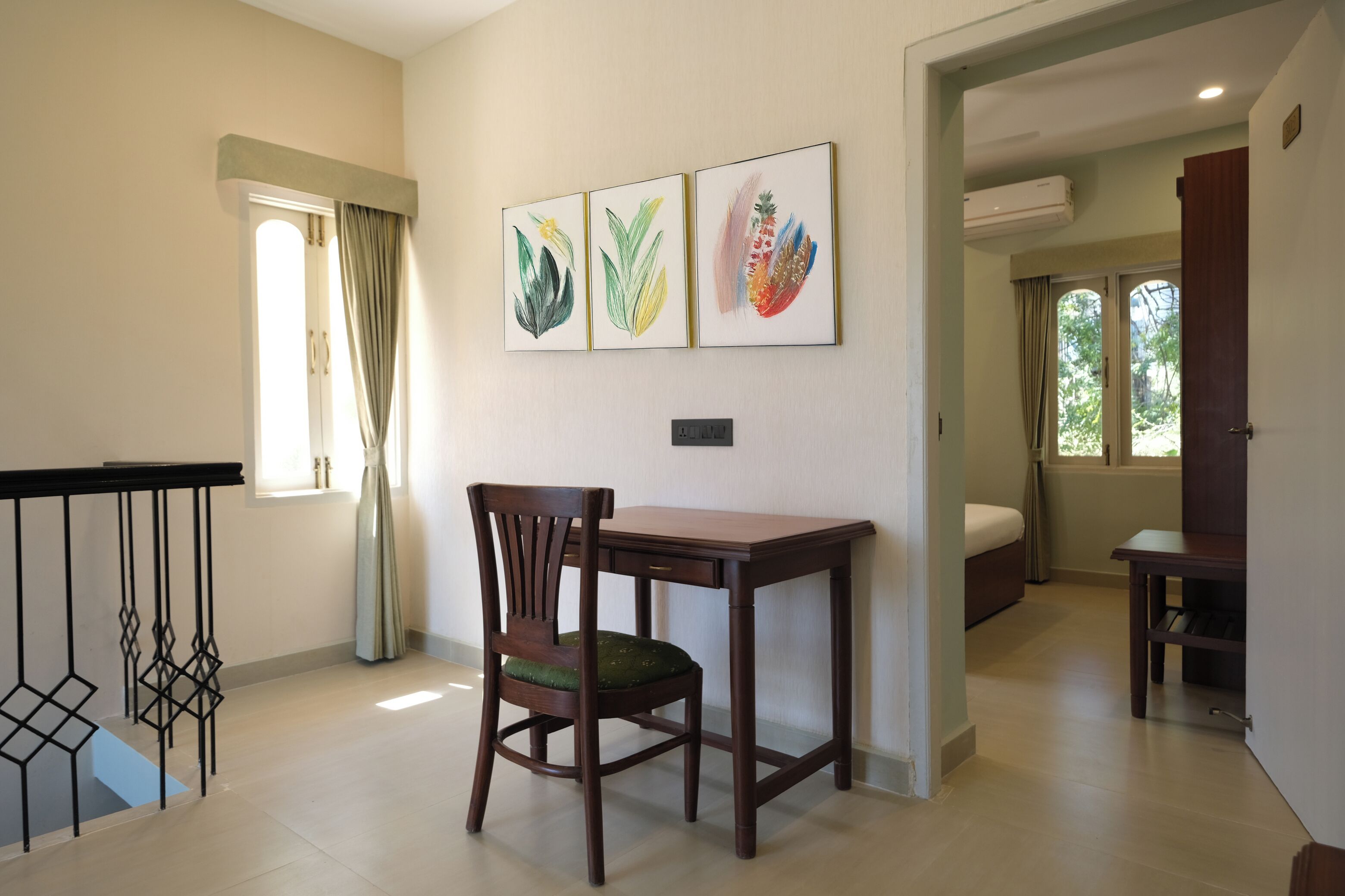 A dining area with a wooden table and chair, a window with curtains, and three framed artworks on the wall.