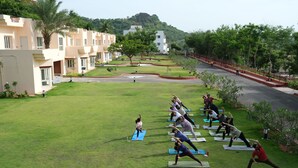 A group of people practicing yoga on a grassy lawn with buildings in the background. - Kyra Wellness Resort (Hyderabad)