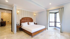 A spacious bedroom with a large bed, a nightstand, a desk, and a window with curtains. - Kyra Wellness Resort (Hyderabad)