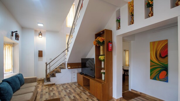 Een moderne woonkamer met een trap, houten vloeren, een bank, een televisie en een schilderij.