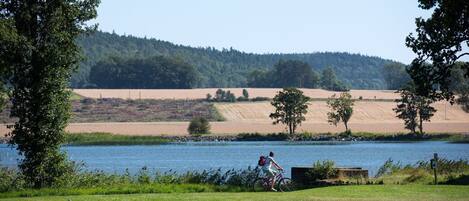 Une personne à vélo, près d’un lac, avec une colline boisée en arrière-plan.
