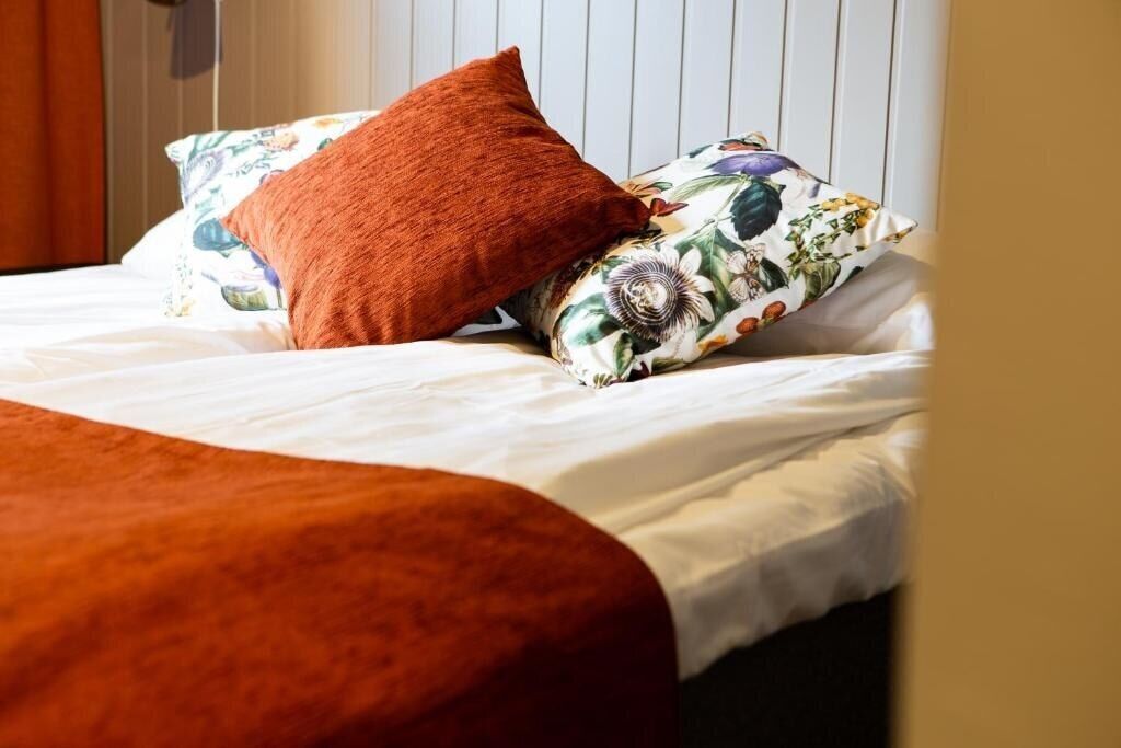 A bed with white bedding, a brown throw blanket, and floral-patterned pillows.