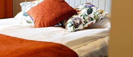 A bed with white bedding, a brown throw blanket, and floral-patterned pillows.