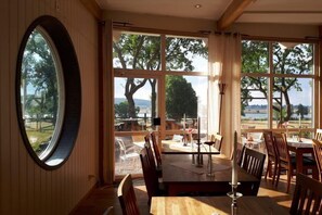 A dining area with large windows, wooden furniture, and a view of the outdoors. - Hotell Hehrne  (Vanersborg)