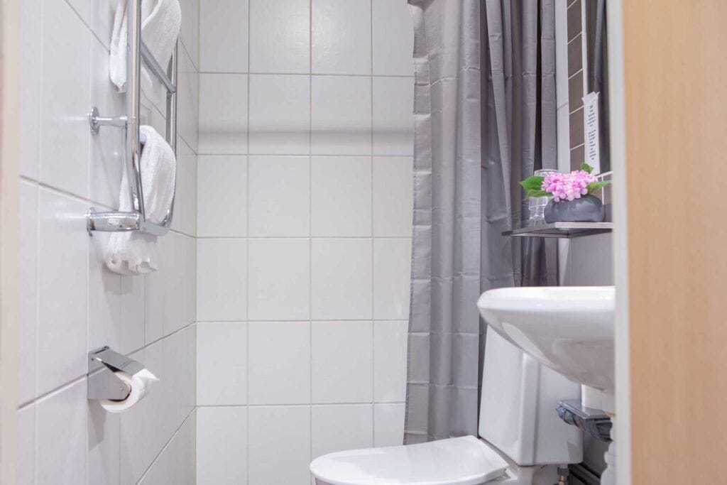 A bathroom with white tiles, a toilet, a sink, a towel rack, and a shower curtain.