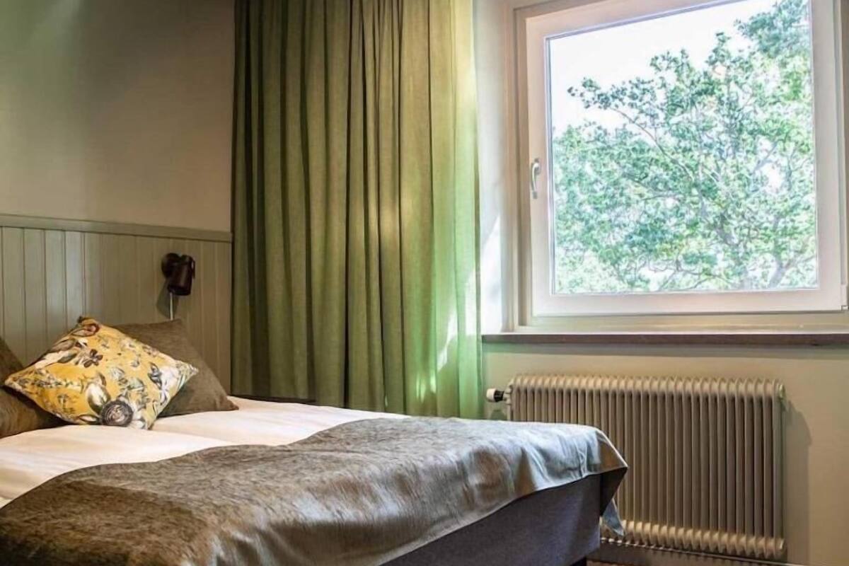 Une chambre à coucher avec un lit, une fenêtre donnant sur des arbres et un radiateur.