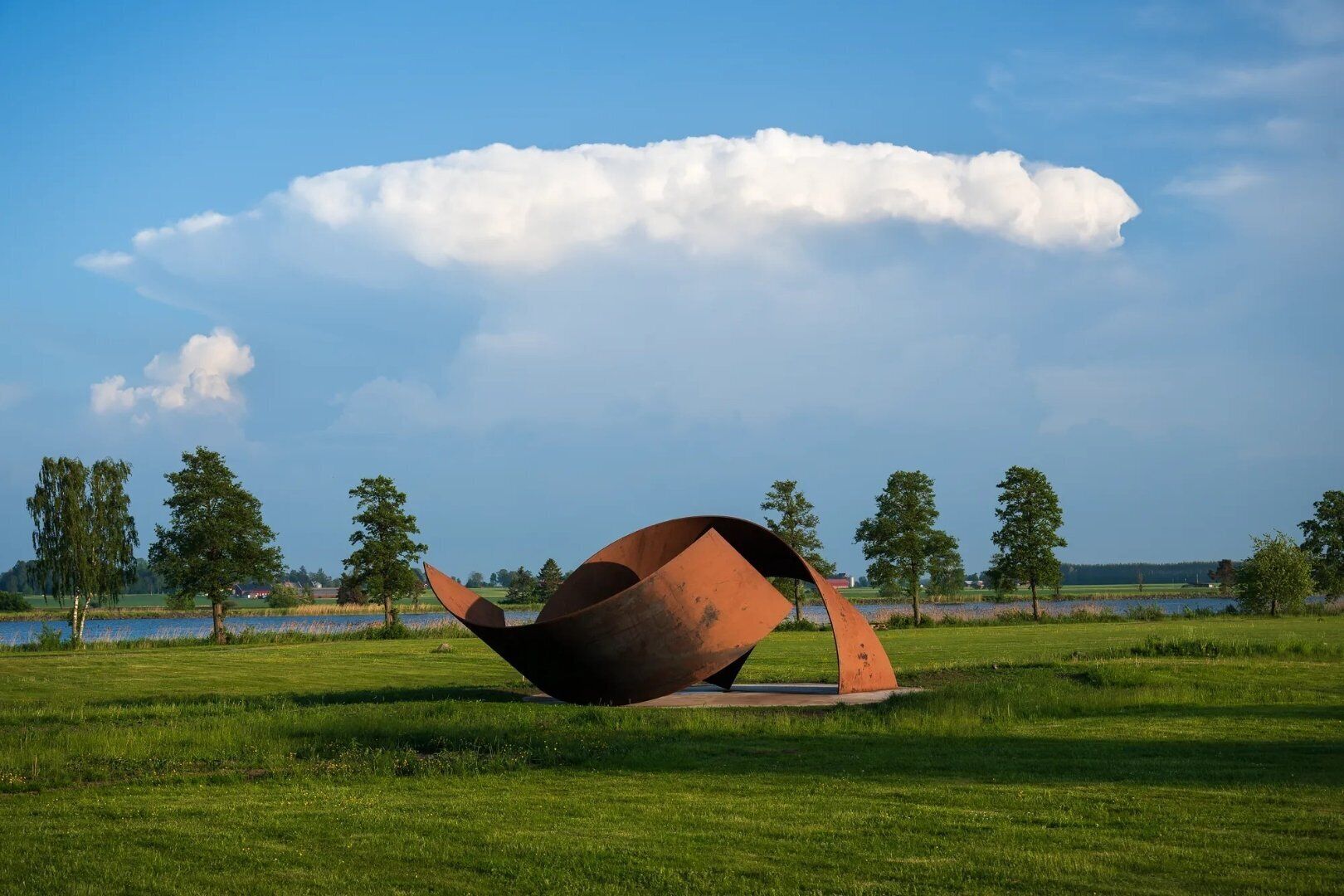 A sculpture in a grassy field with a lake and trees in the background.