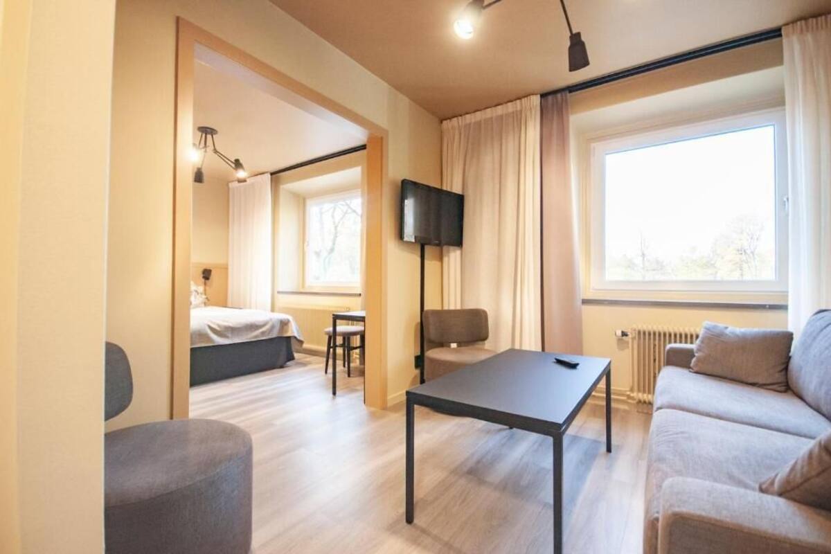 Une chambre d’hôtel moderne équipée d’un lit, d’un canapé, d’une table, d’une télévision et d’une fenêtre avec des rideaux.