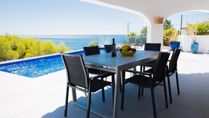 Un espace extérieur aménagé pour les repas, avec vue sur la mer, une piscine et des plantes en pot.
