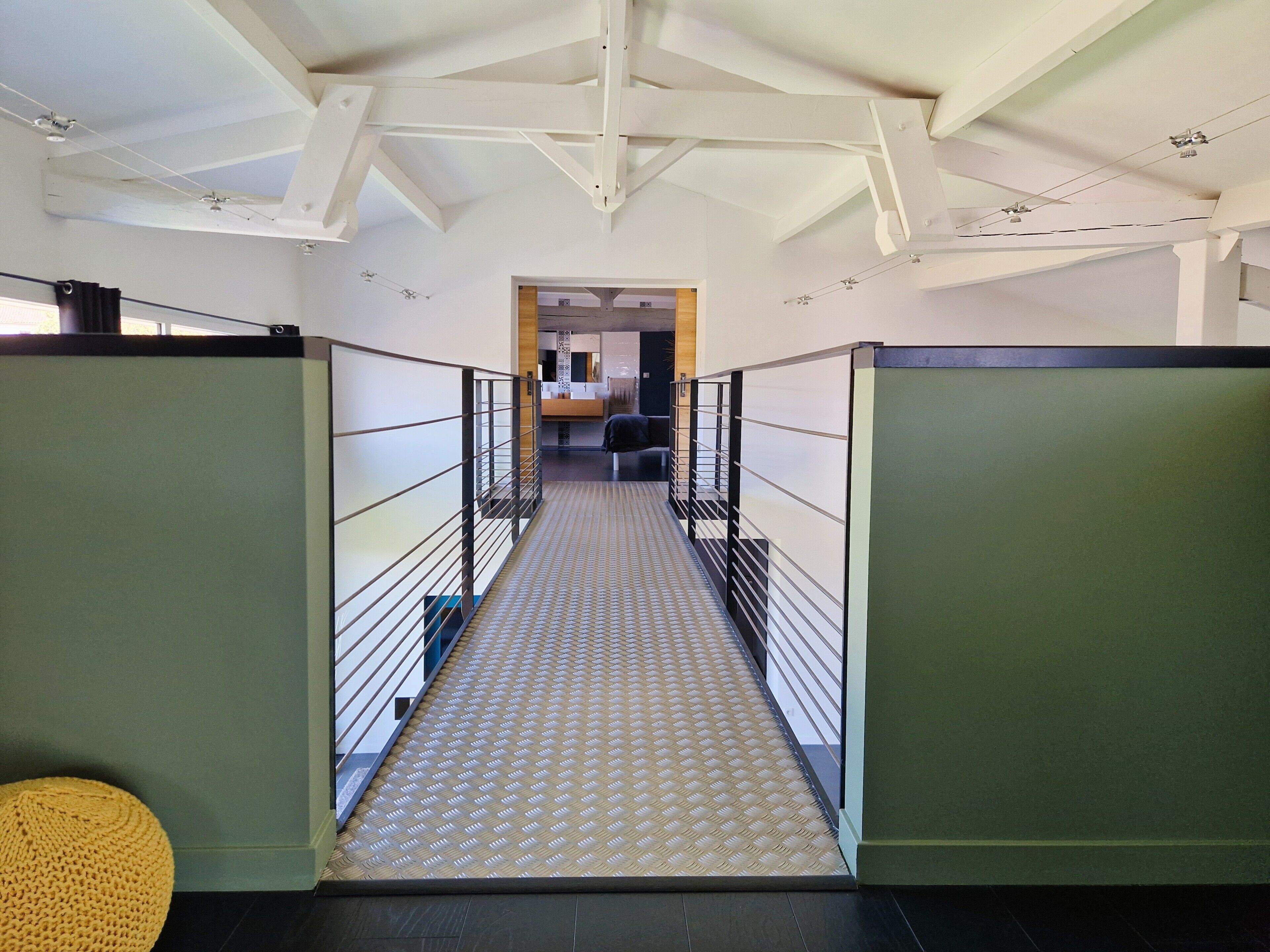 A hallway with a patterned floor, metal railings, and a ceiling with exposed beams.