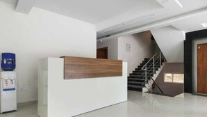Un espace d’accueil avec un comptoir blanc et un panneau en bois, un distributeur d’eau et un escalier menant à un autre étage.