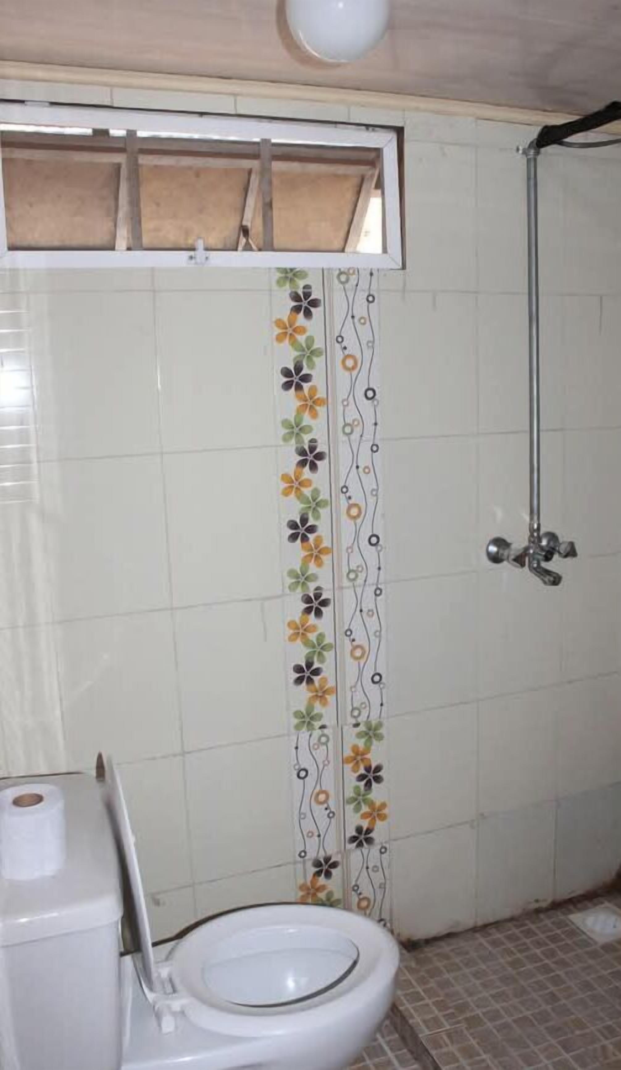 A bathroom with a toilet, a shower, and a decorative floral tile strip.