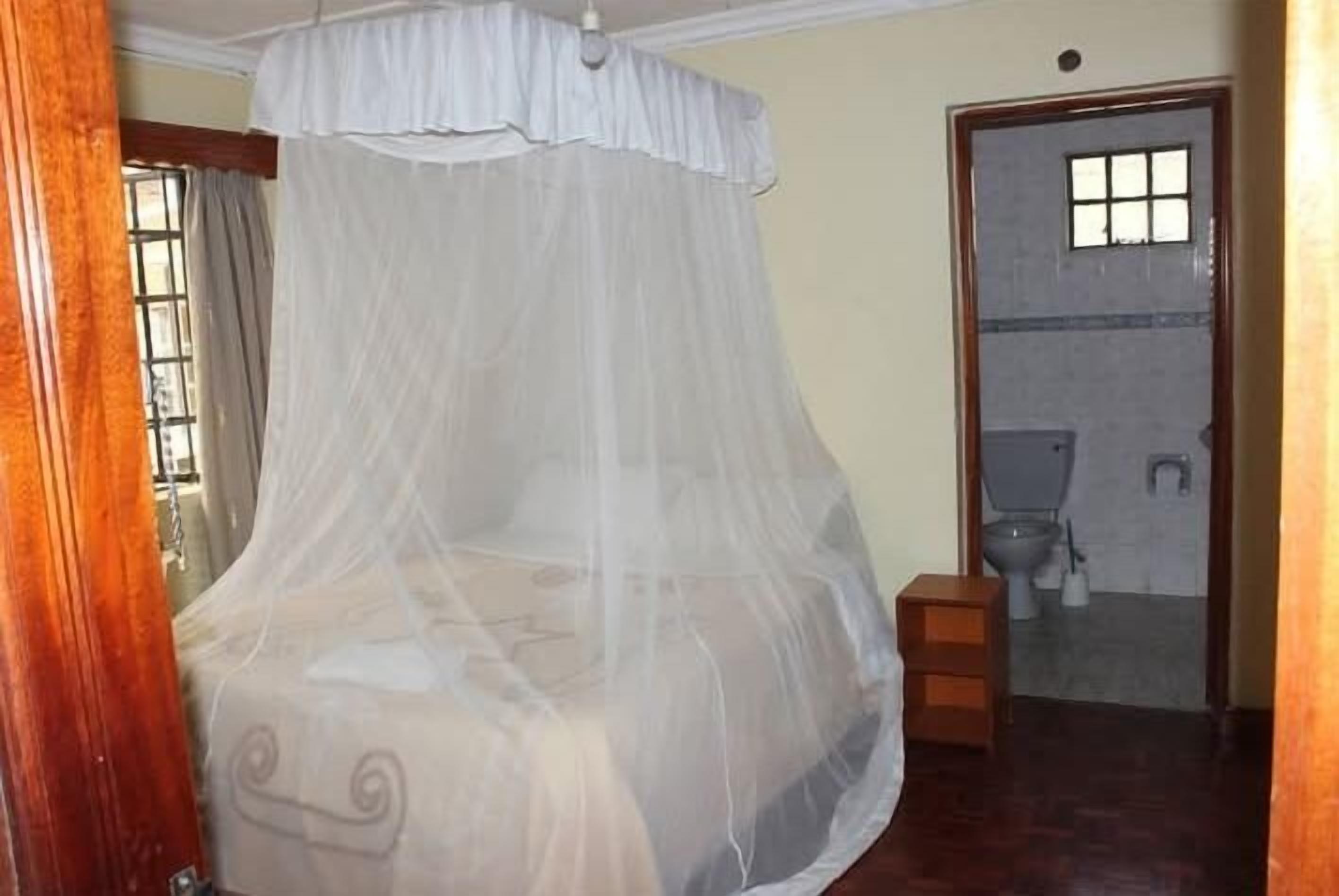 A room with a bed under a white canopy, a wooden bench, and a bathroom visible through an open door.