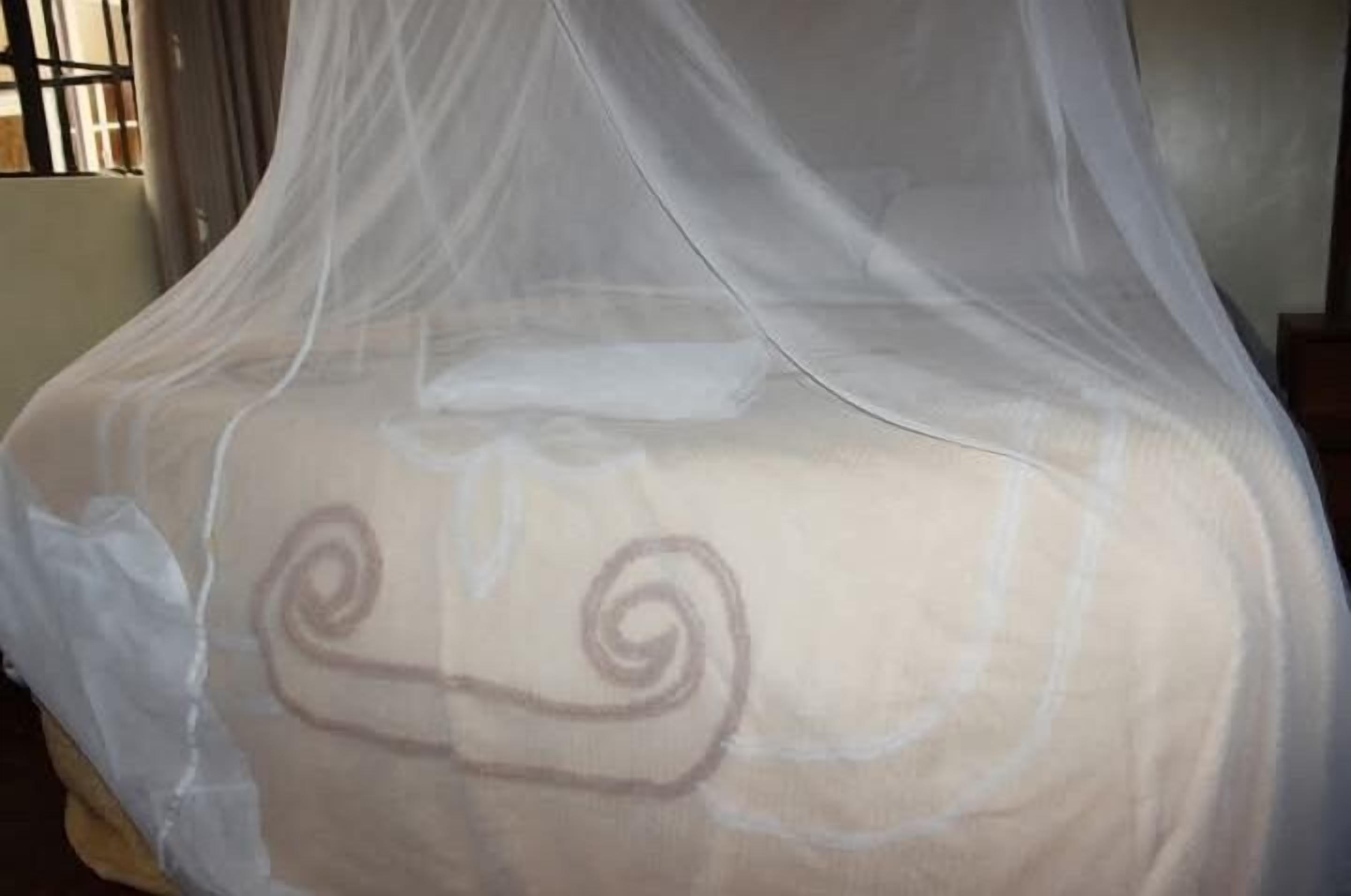 Una cama con cubrecama blanco y un estampado decorativo en espiral, cubierta por un dosel blanco translúcido.
