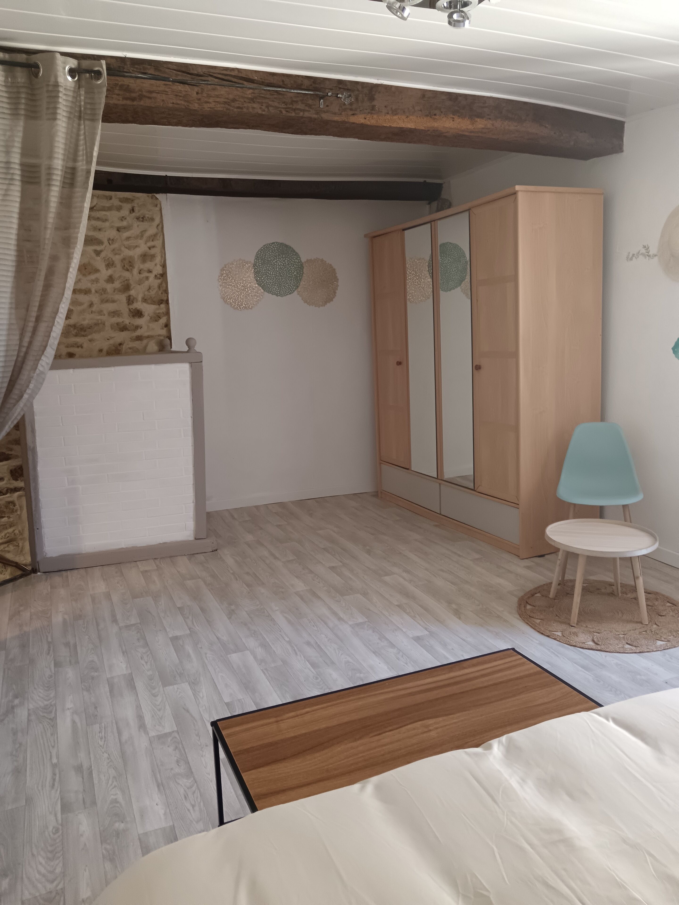 Een slaapkamer met een bed, een kledingkast, een stoel en een klein tafeltje.
