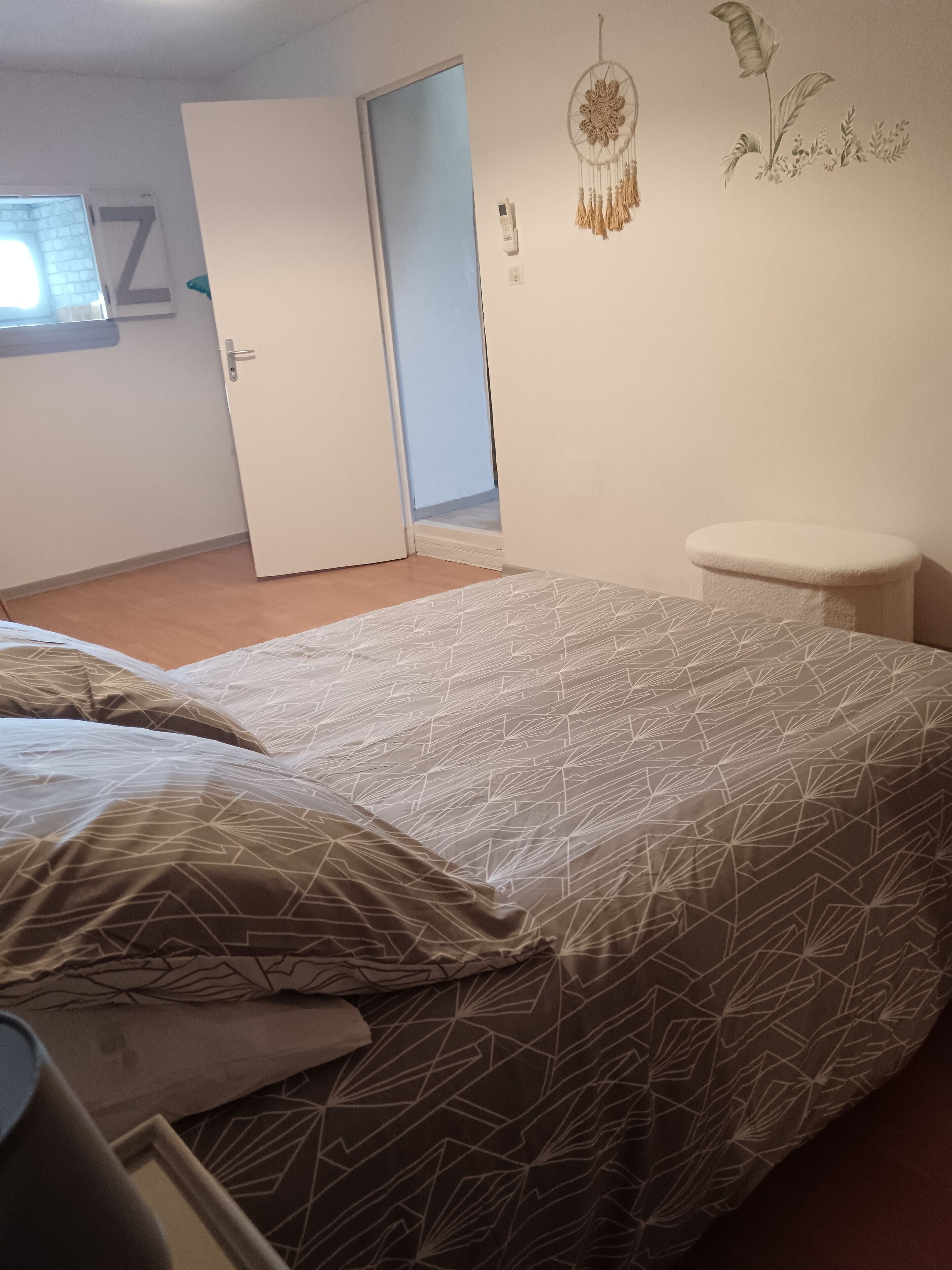A bedroom with a bed, a nightstand, a wall-mounted dreamcatcher, and a door leading to another room.