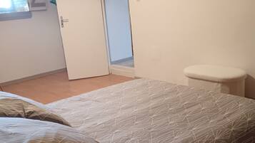 A bedroom with a bed, a nightstand, a wall-mounted dreamcatcher, and a door leading to another room.
