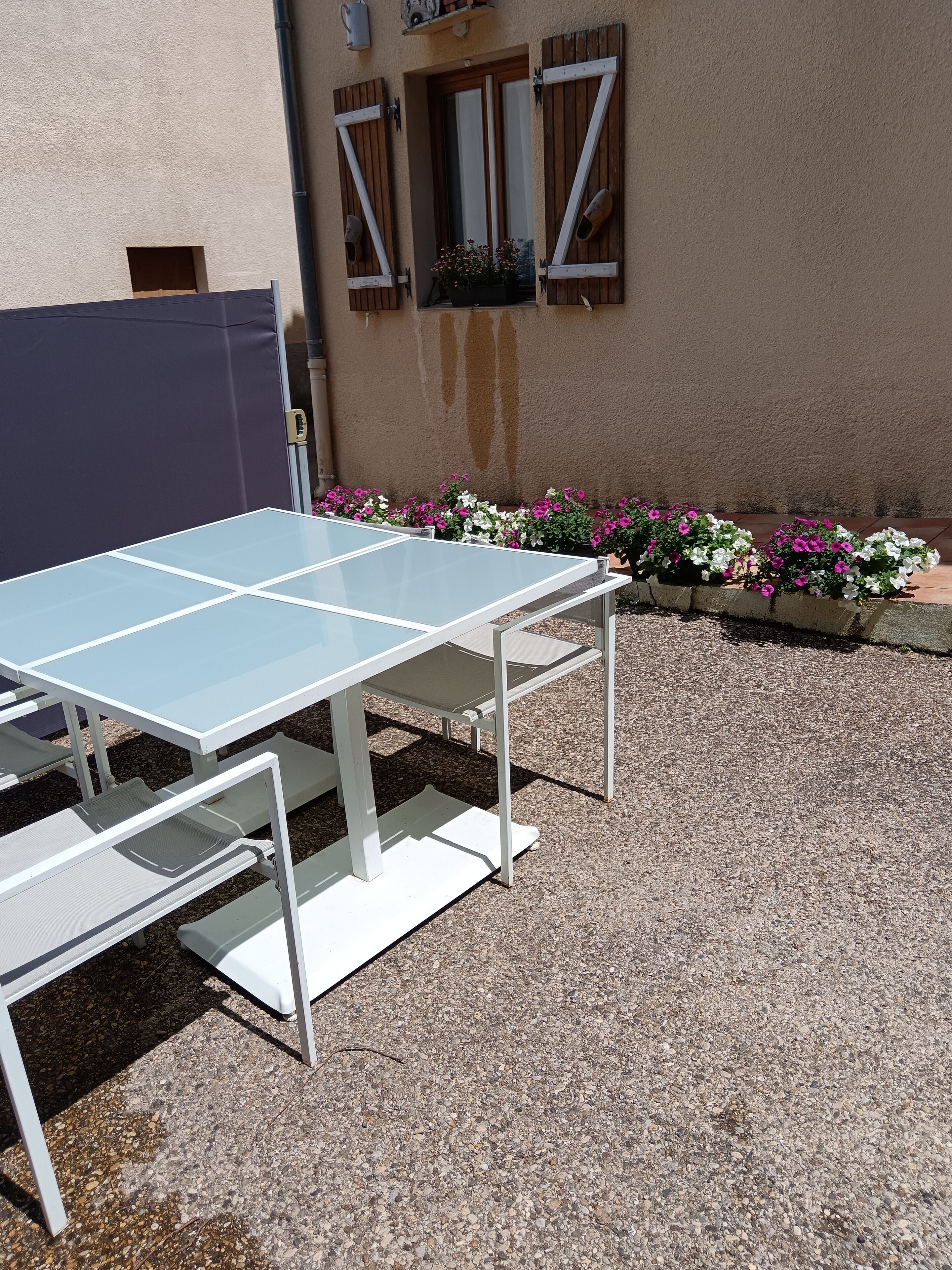 Una mesa de ping pong con bancos, frente a un edificio con pared texturizada y jardineras.