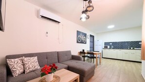 A modern living room with a grey sofa, a wooden coffee table with a potted plant, and a dining area with a small table and chairs. - Adi Hacarmel (Daliyat al-Karmel)