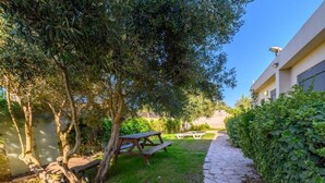 A garden area with a stone pathway, picnic tables, and a building in the background. - Adi Hacarmel (Daliyat al-Karmel)