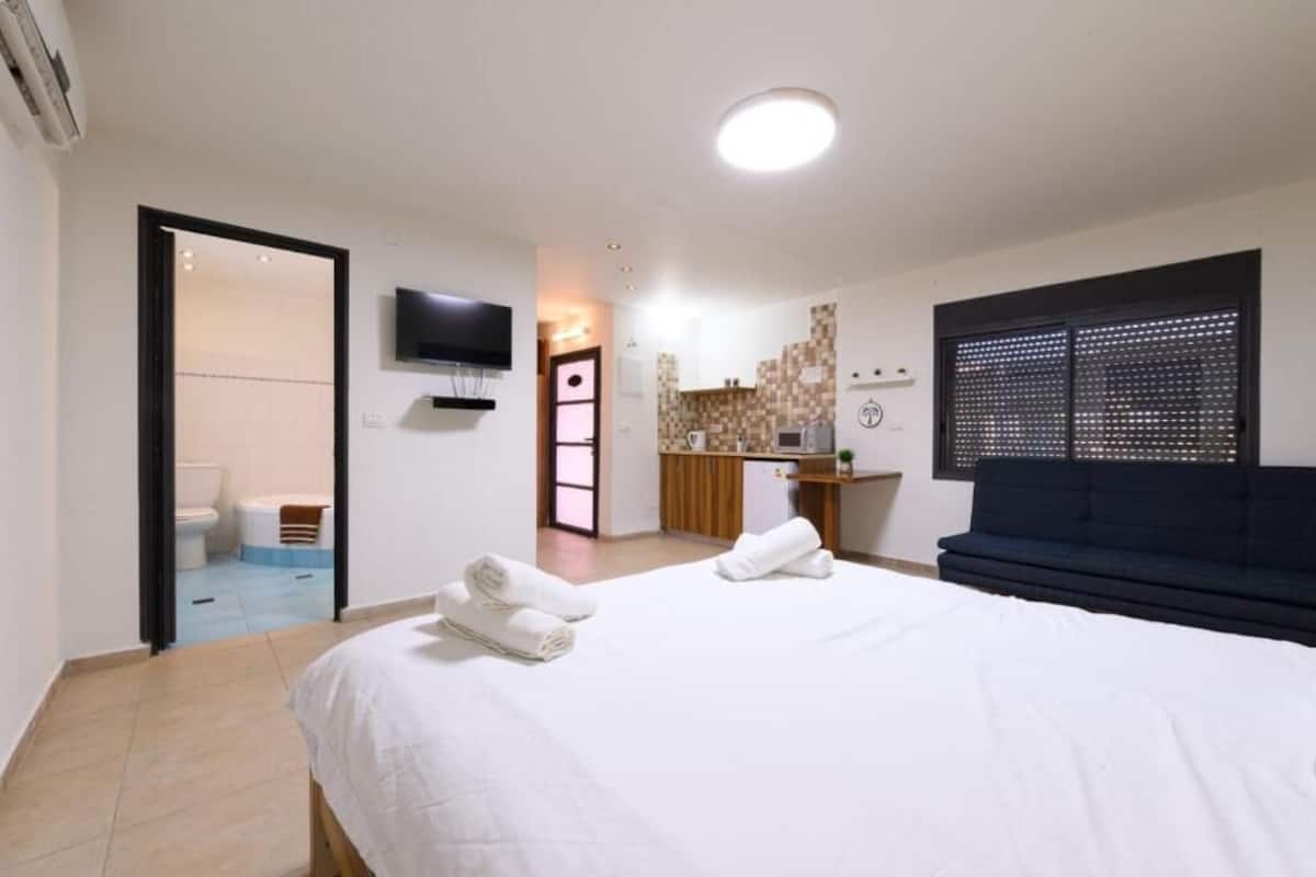 Ett hotellrum med en säng, en tv, ett litet kök och ett badrum som syns genom en öppen dörr.
