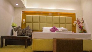 A hotel room with a large bed, a bedside table, a small table, and a decorative plant. - Grand Plaza Hotel (Dhaka)
