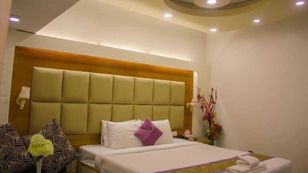 A hotel room with a large bed, a headboard, a bedside table, a lamp, and a flower arrangement. - Grand Plaza Hotel (Dhaka)