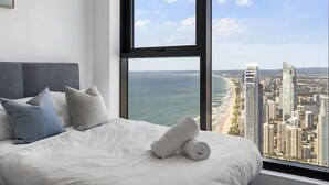 A hotel room with a large window offering a view of a city skyline and the ocean.